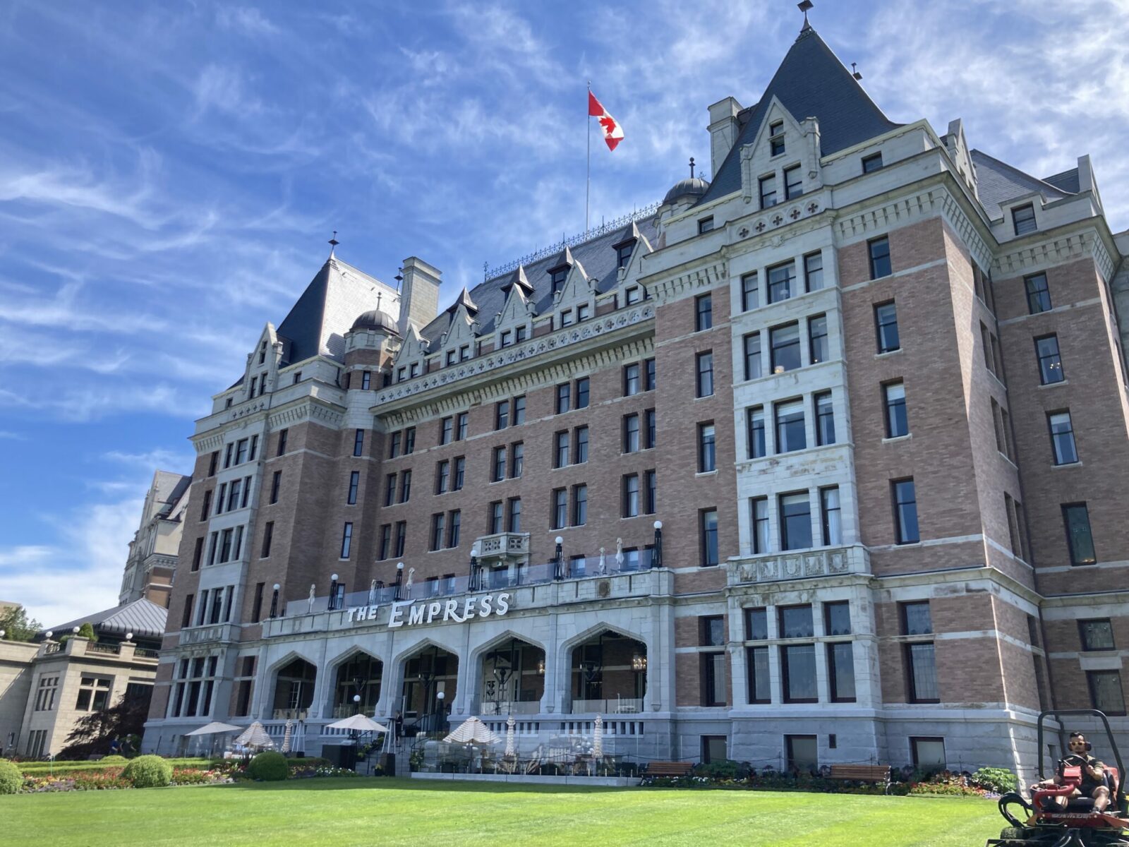 The exterior of the Empress hotel in Victoria BC. It's a brick building with a verandah and lawn in front and a Canadian flag flying overhead.