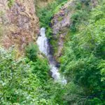 Thunderbird Falls going down about 200 feet through a rocky canyon lined with green trees and shrubs
