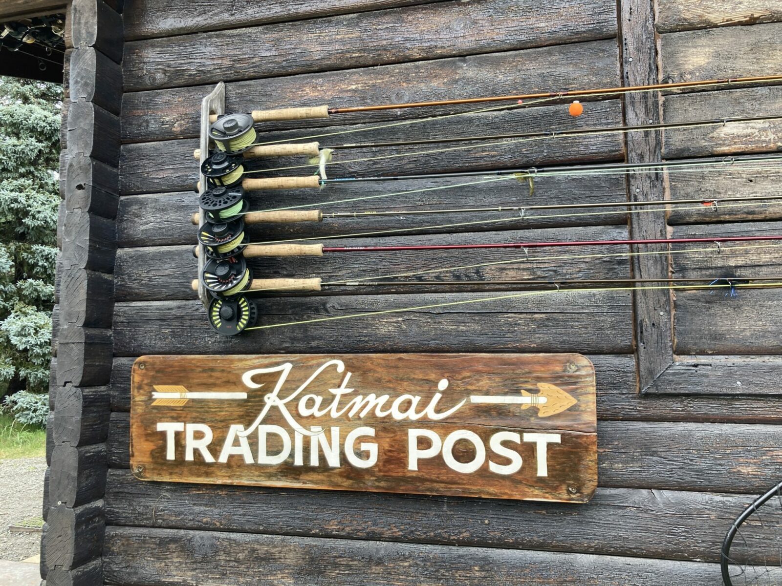 A wooden building with fishing rods on the side above a sign that says Katmai Trading post