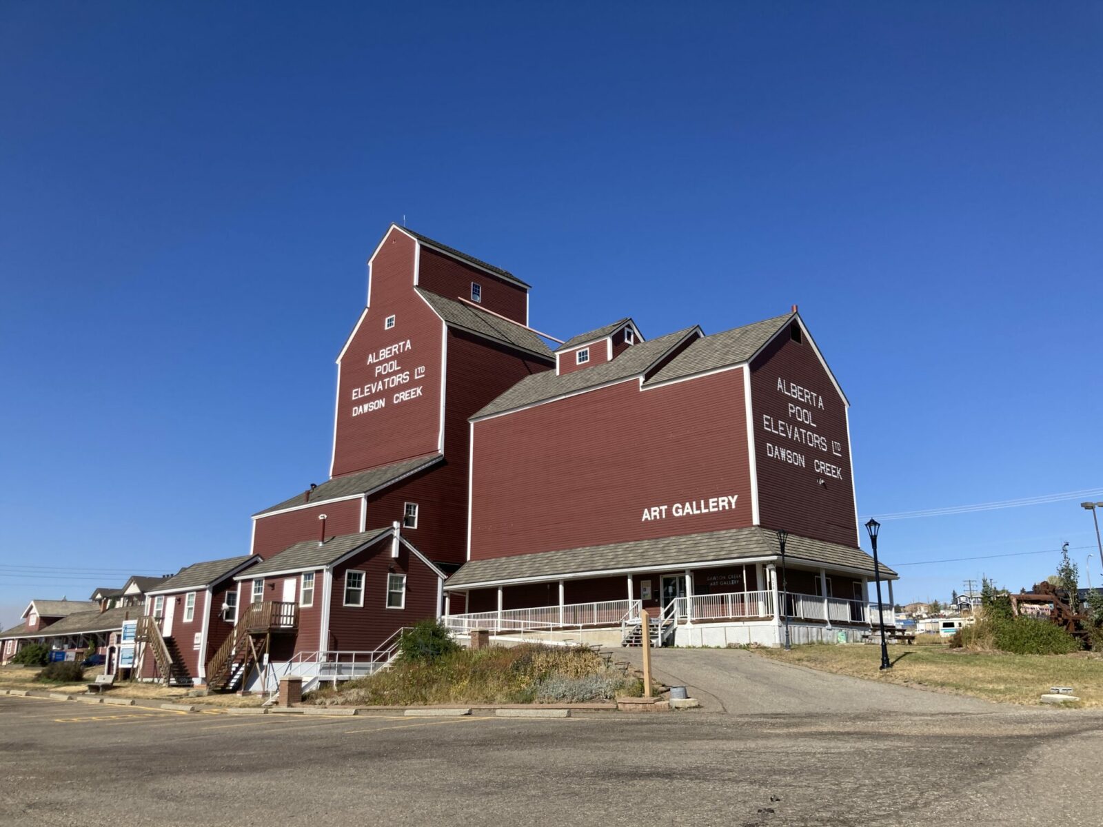 A bright red building with white trim that is a former grain elevator. Now it is an art gallery and in white letters on the side is painted Alberta pool elevators Dawson Creek art gallery