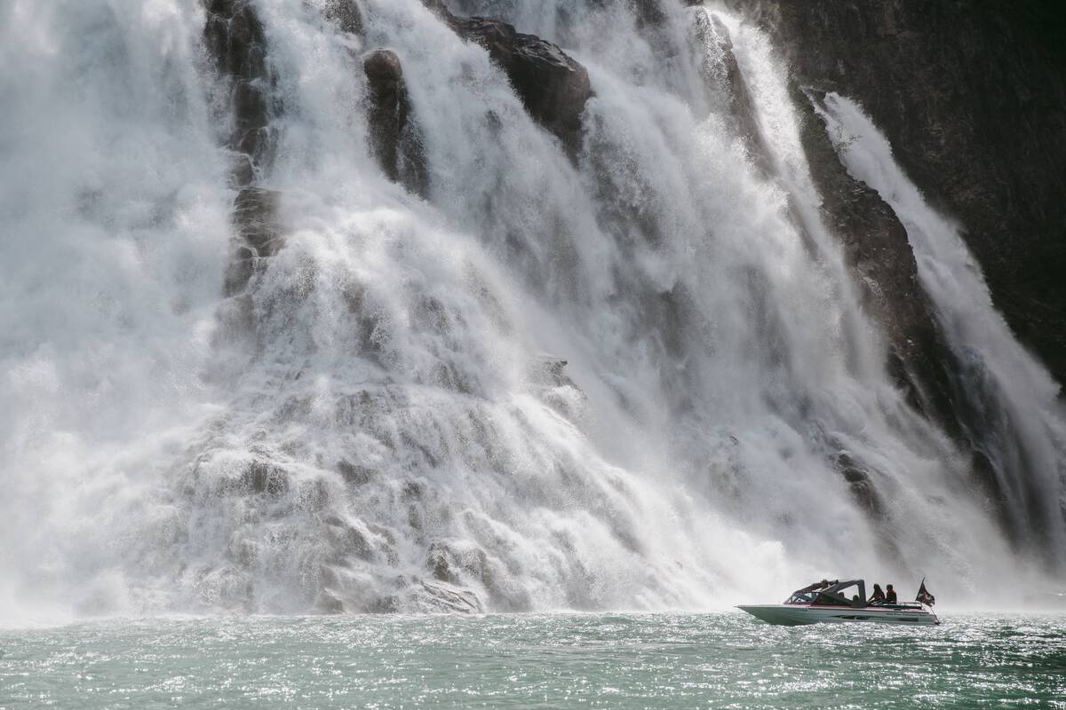 The base of stunning Kinuseo Falls, a 225 foot high waterfall near Tumbler Ridge BC. There is a jetboat at the base of the falls near the spray and a bit of the river below is visible