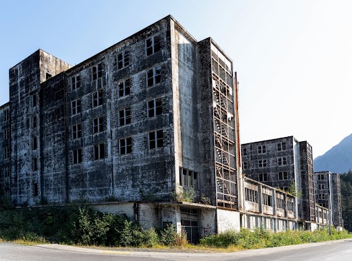 An abandoned building with green bushes growing around it. It's a four story building with empty windows