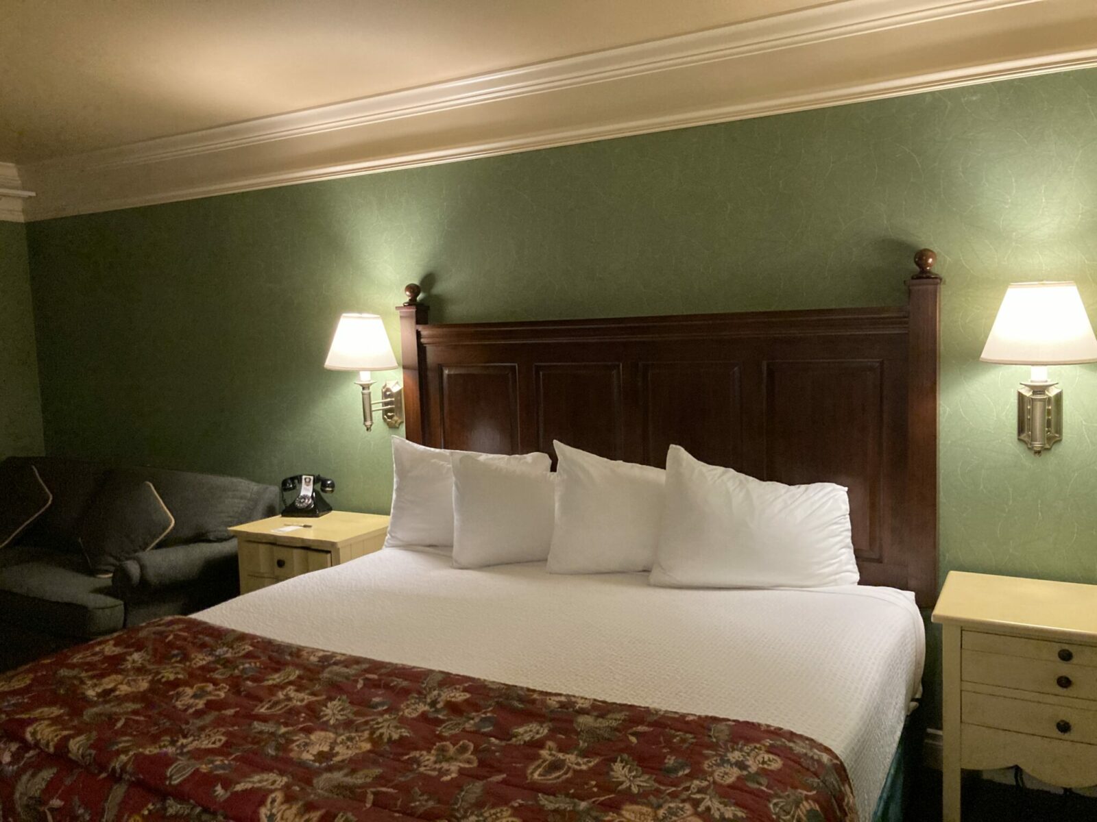 A King Size bed with a wooden headboard and 4 white pillows. There are two lamps on each side of the bed and the wall behind is light green