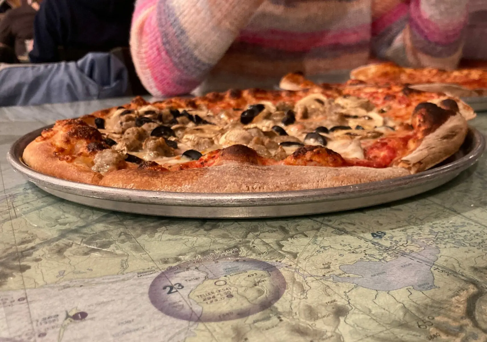 A wood fired pizza on a table that is decorated with aviation charts