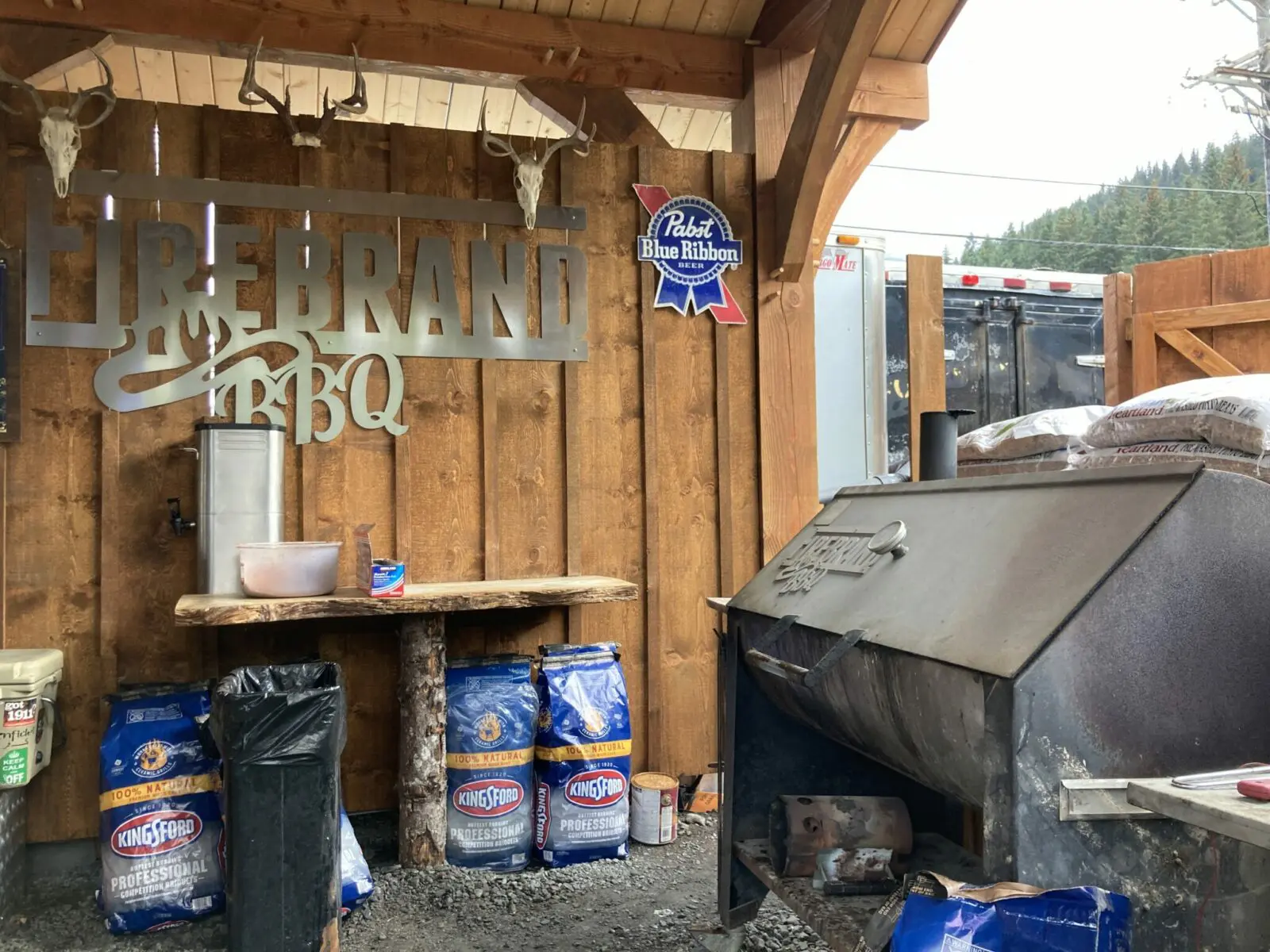 An outdoor bb1 with a huge smoker and lots of charcoal bags around it