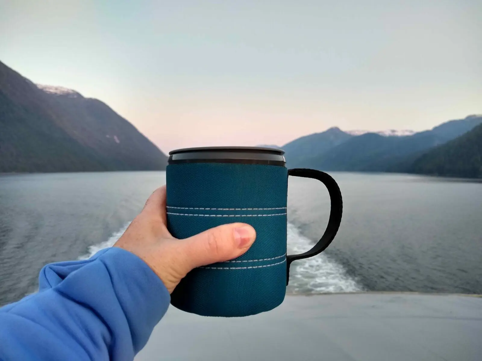 A person's hand holing up a mug at the back of a ship