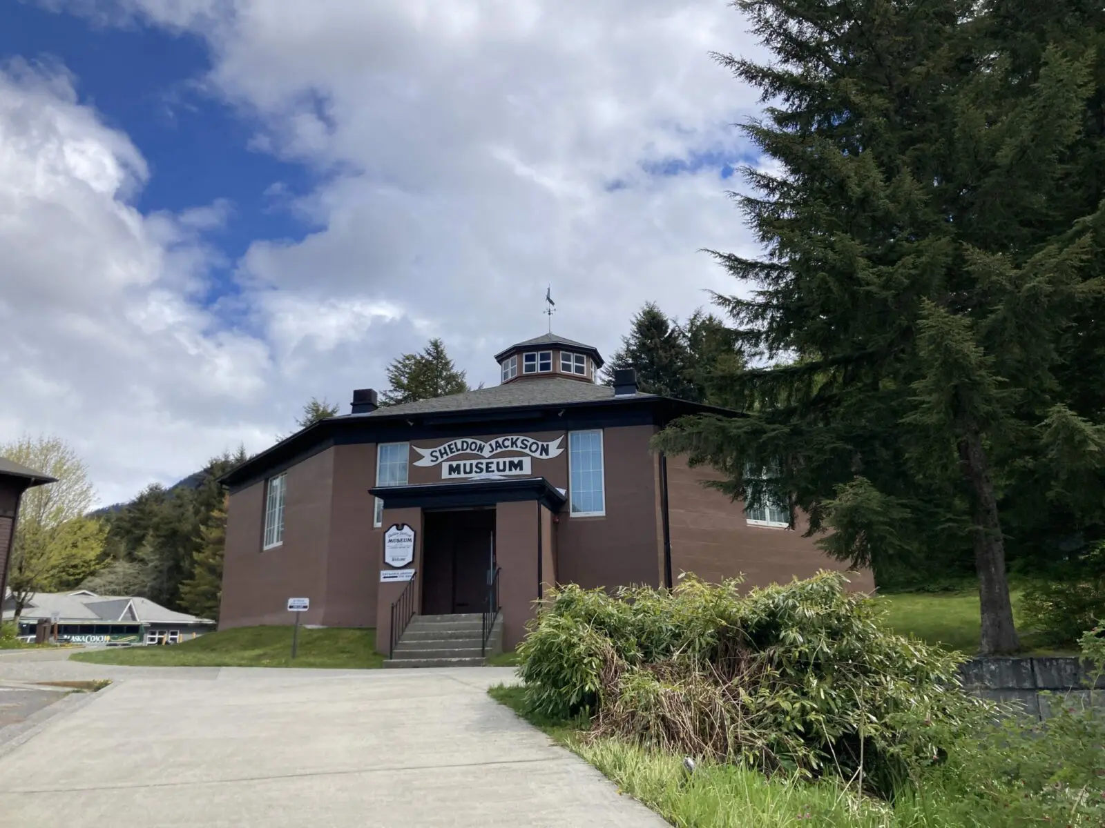 A wooden octagonal brown building surrounded by trees. Sign says Sheldon Jackson Museum