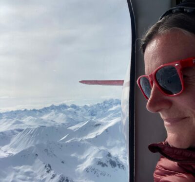 Jennie's head at the window of a flightseeing plane, looking out at the mountains below the plane