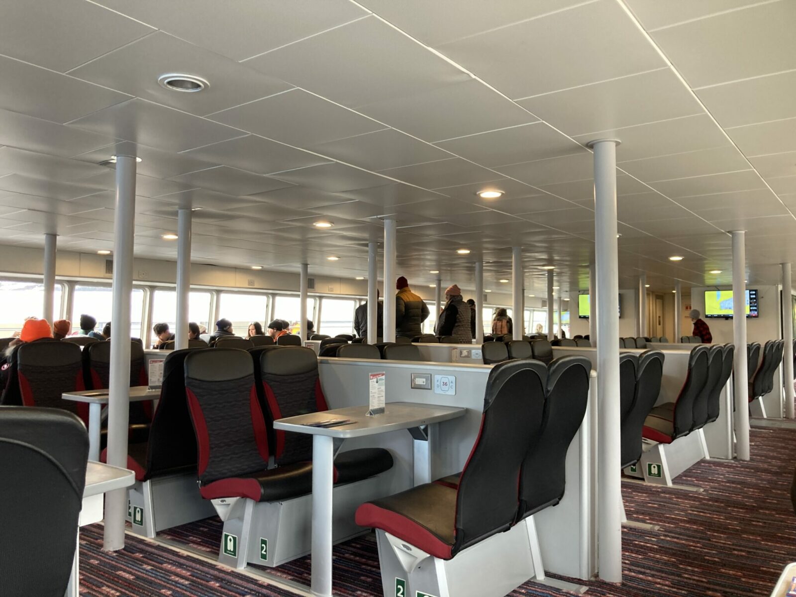 The interior of a boat with lots of tables with four chairs and a few people standing around