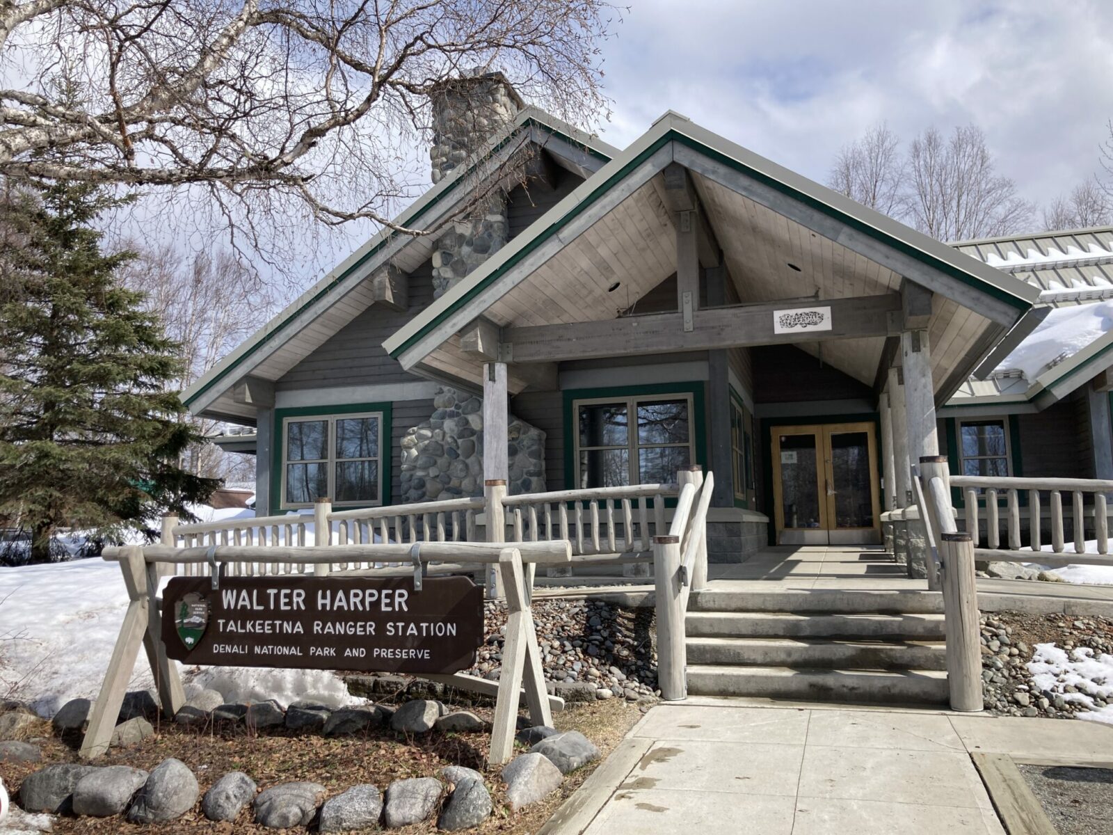 The outside of a wood and stone ranger station. The sign in front says Walter Harper Ranger Station Talkeetna Alaska