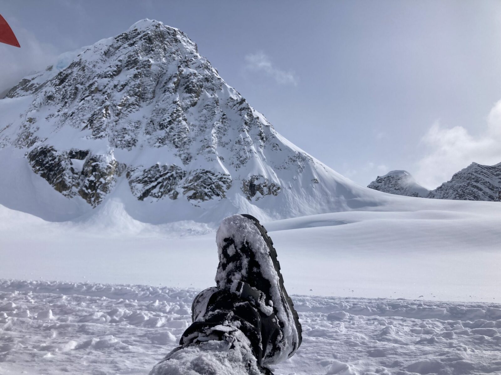 A person's feet in black glacier boots on a glacier surrounded by mountains in Denali National Park