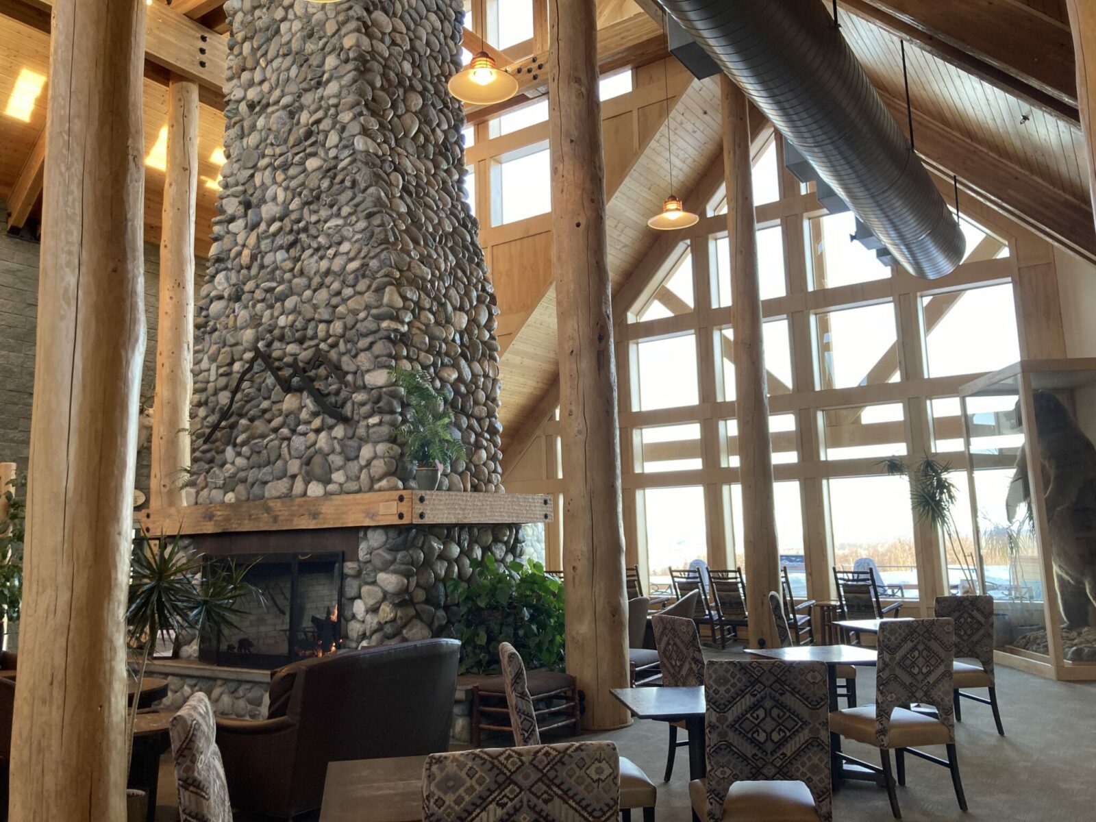 A stone fire place and tables and chairs near giant windows.