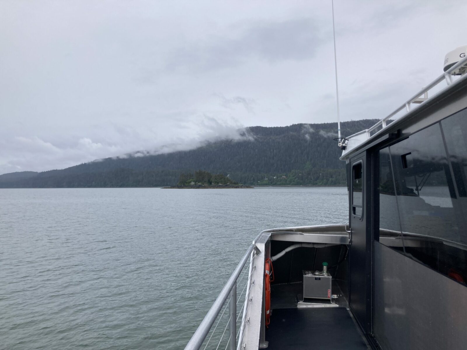 The side of a tour boat with gray water and forested hillsides nearby on a cloudy day.