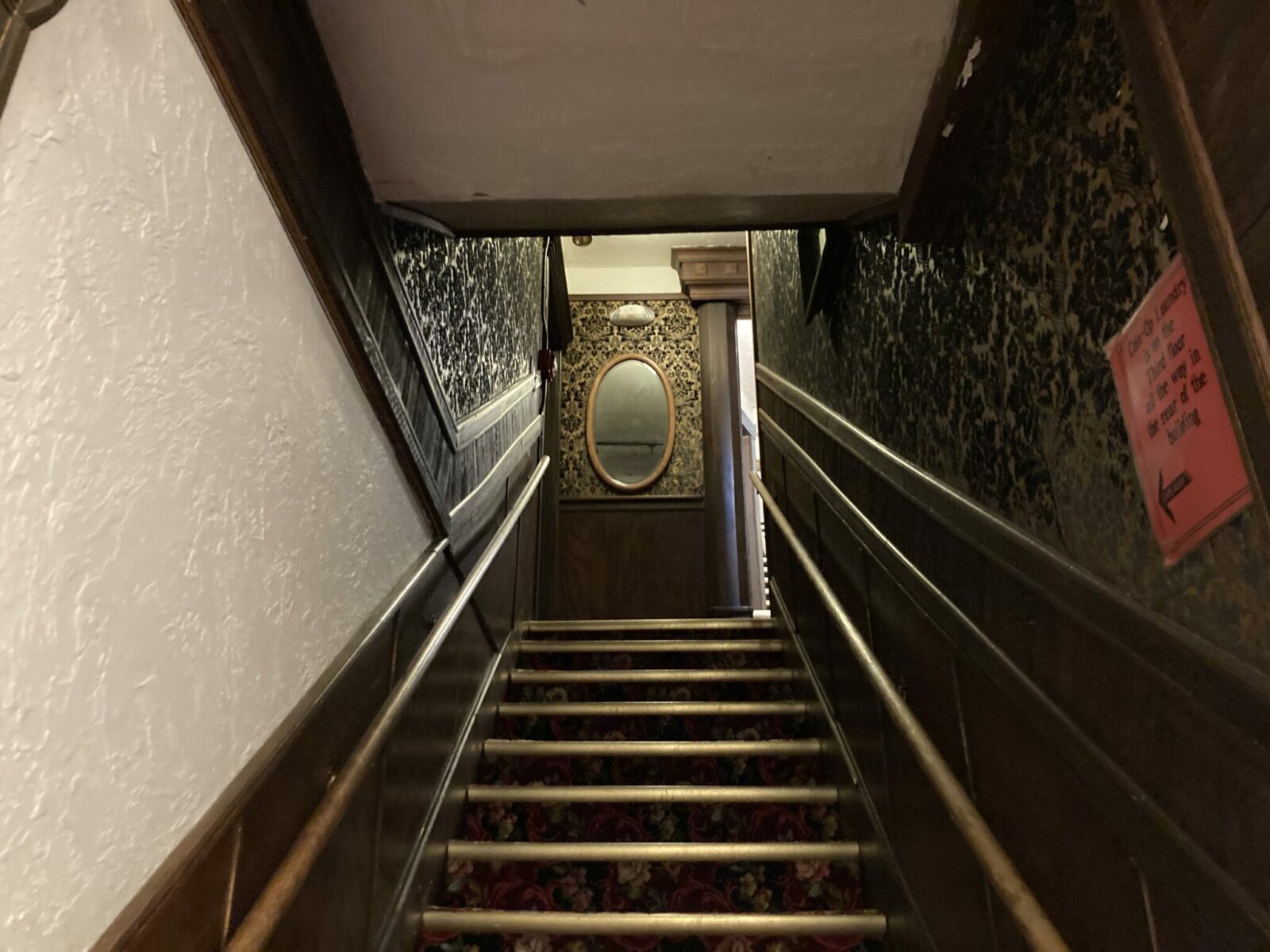 A steep carpeted stairway in a historic building, with Victorian wall paper on the sides of the stairwell