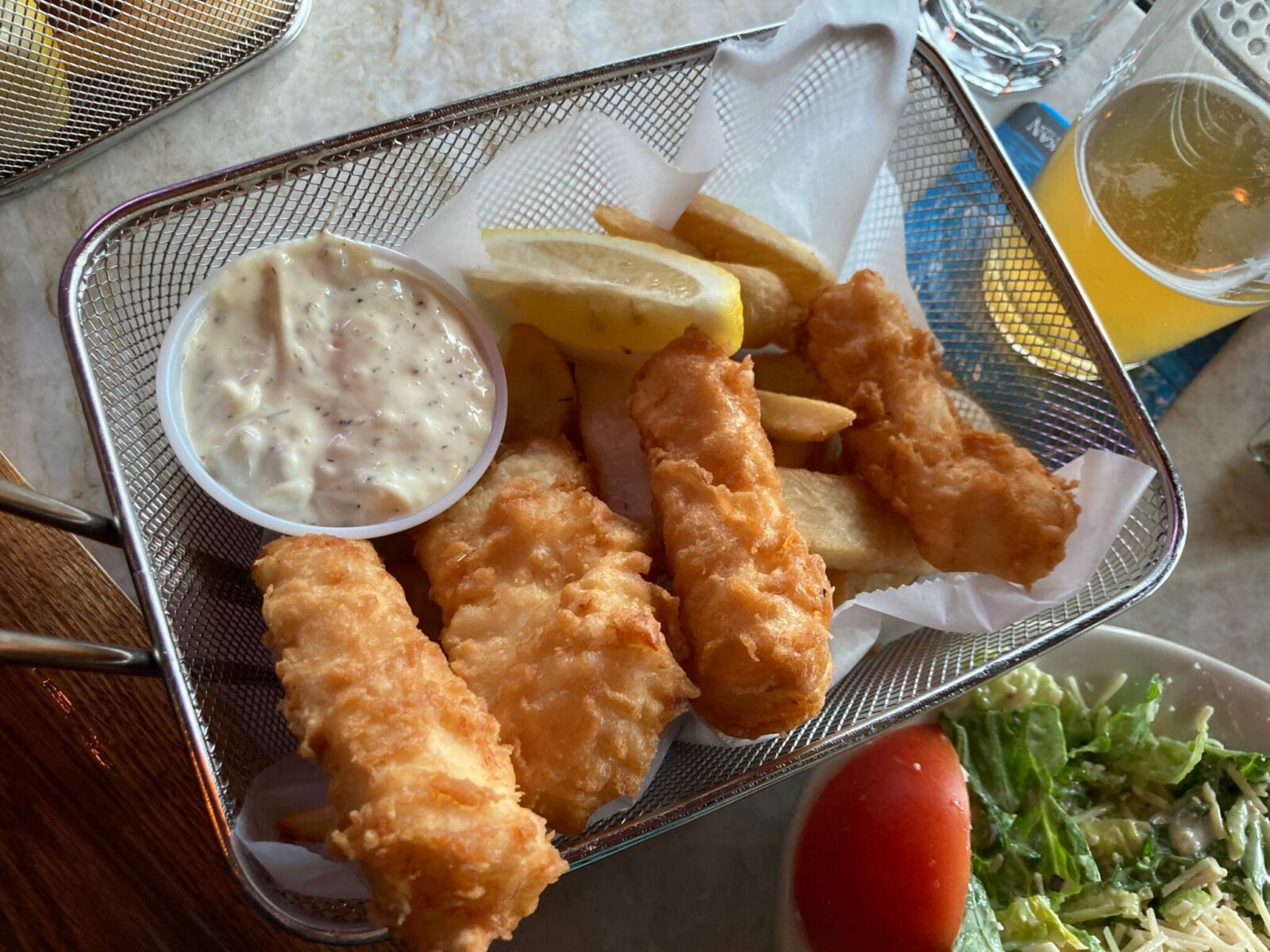 A basket of four pieces of fried fish, french fries, tartar sauce and a beer