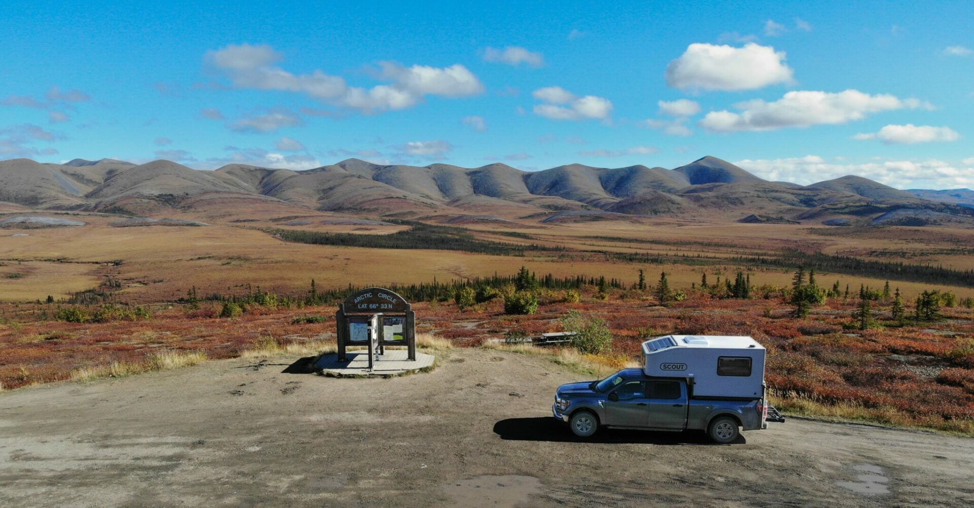 A Scout pick up camper and F150 pick up truck at the Arctic Circle on the dempster highway with fall colors and mountains in the background