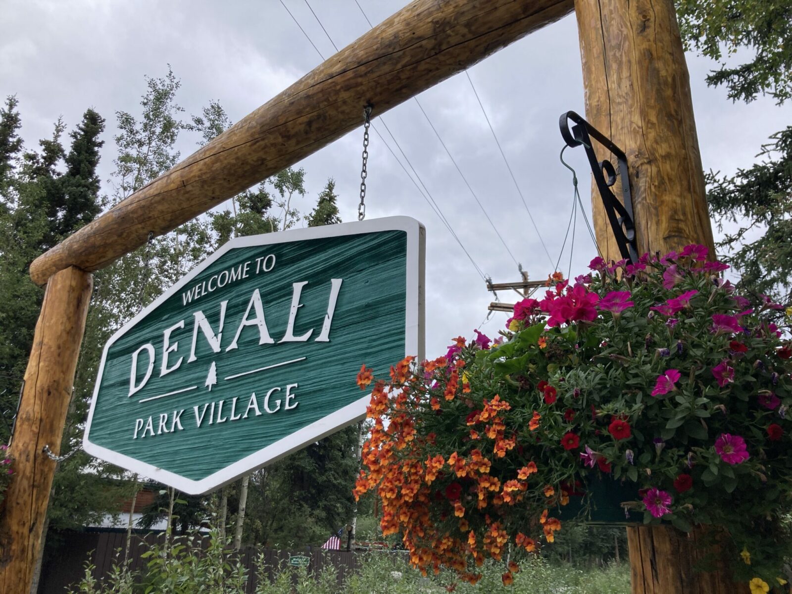 A wooden sign saying welcome to denali park village and a flower basket