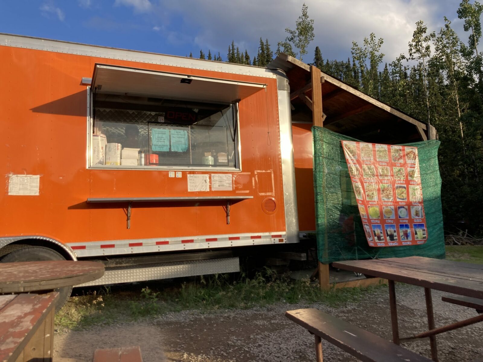 An orange food truck with a photo menu and a picnic table.