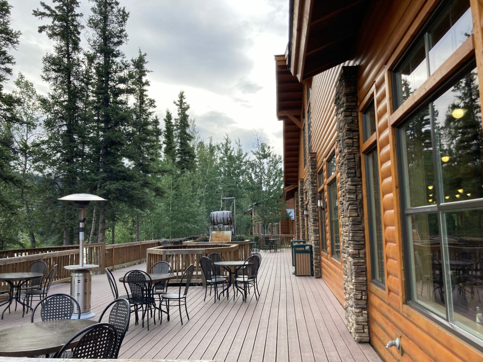 The deck outside the dining room at Denali Park Village. There are chairs and tables and propane heaters next to big interior windows