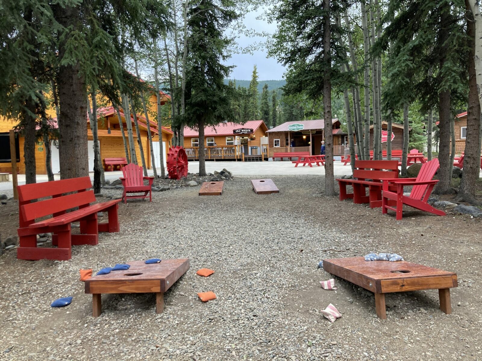 Red chairs and benches between buildings at Denali park village with cornhole