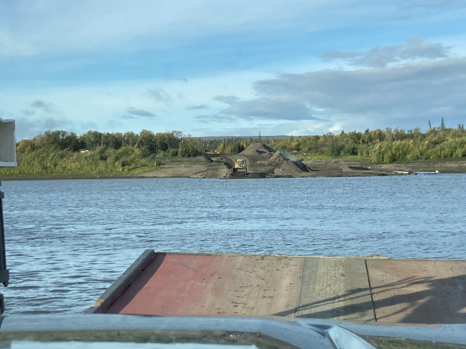 The bow of a ferry on a river with a loader moving gravel at the ferry landing across the river