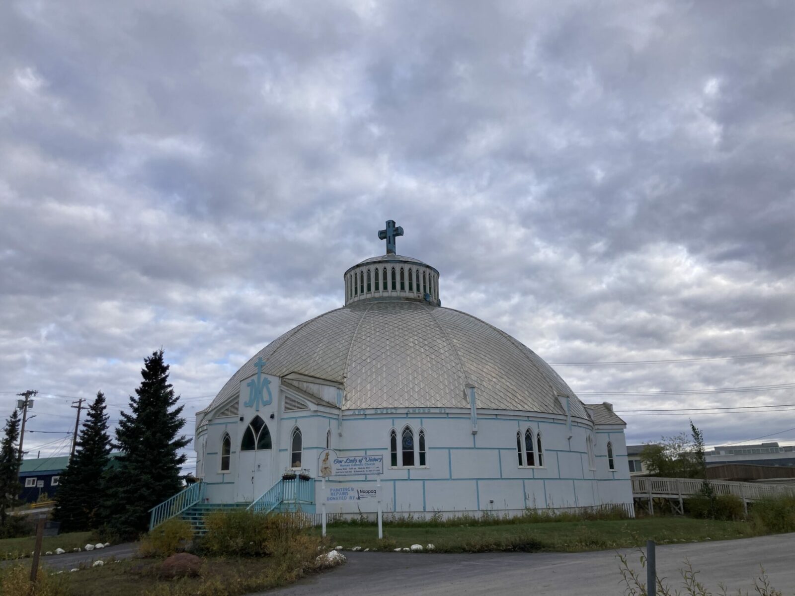 A round white church building with a metal roof and a blue cross on top