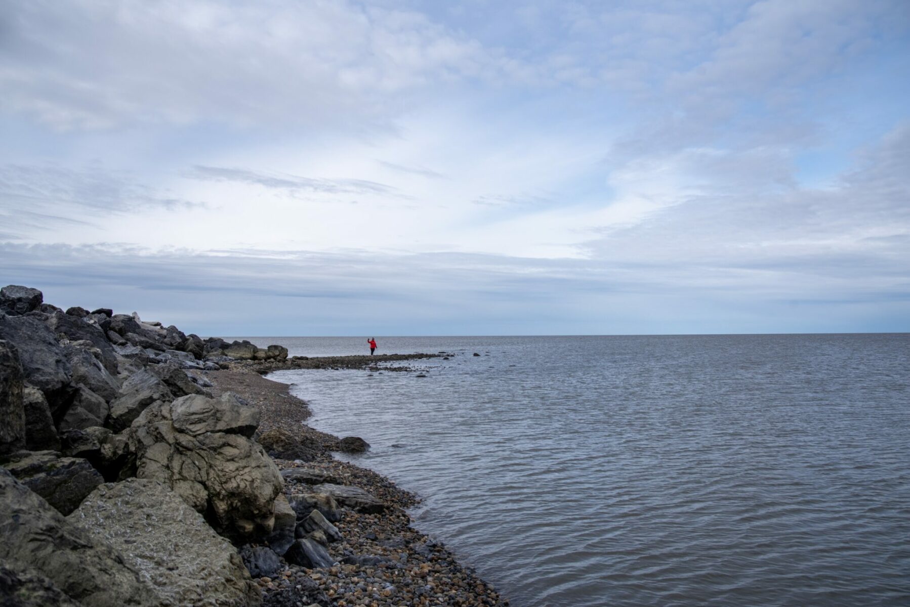 A rocky beach at the Arctic Ocean in Tuktoyaktuk canada, with a person in a red rain jacekt standing along the beach