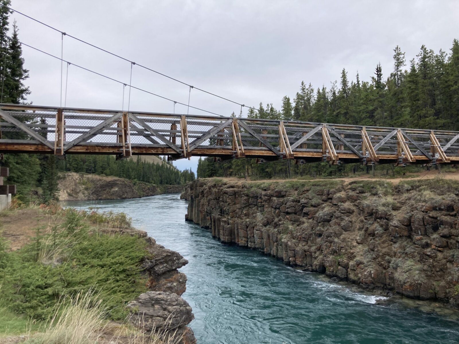 a pedestrian suspension bridge over a narrow rocky canyon with a turquoise river below