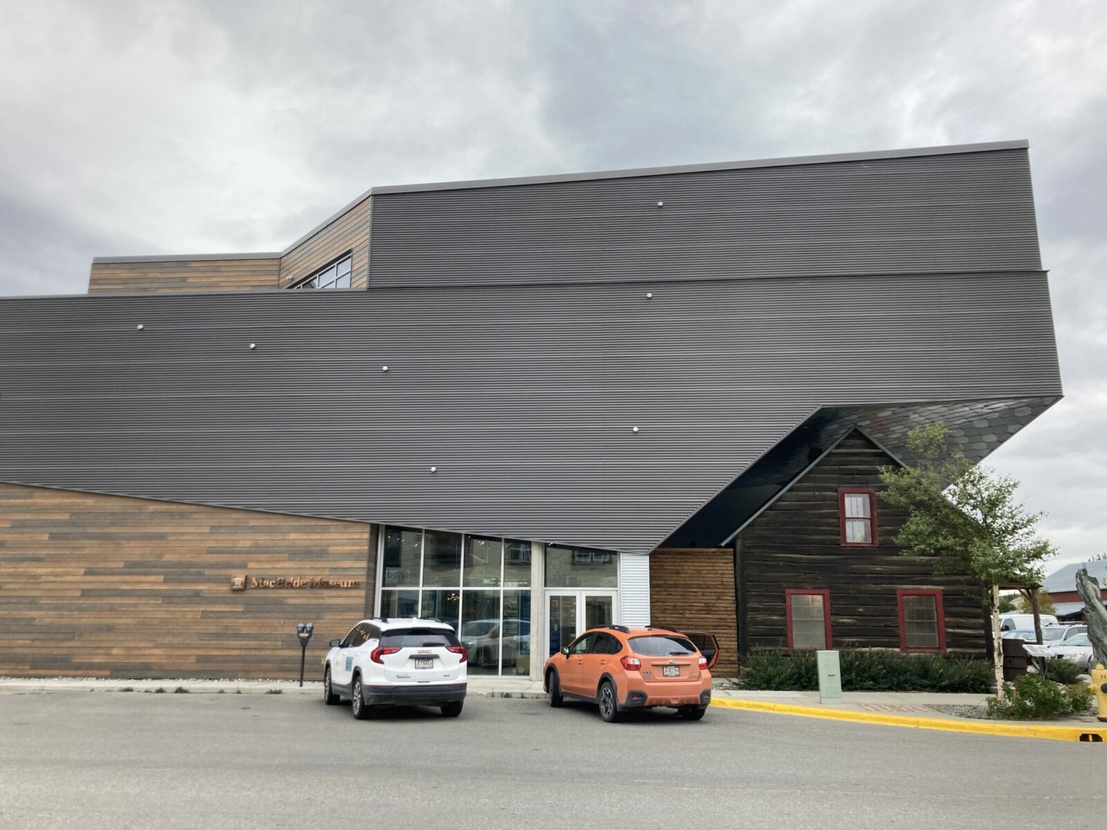 A modern gray building over a small historic wooden building.