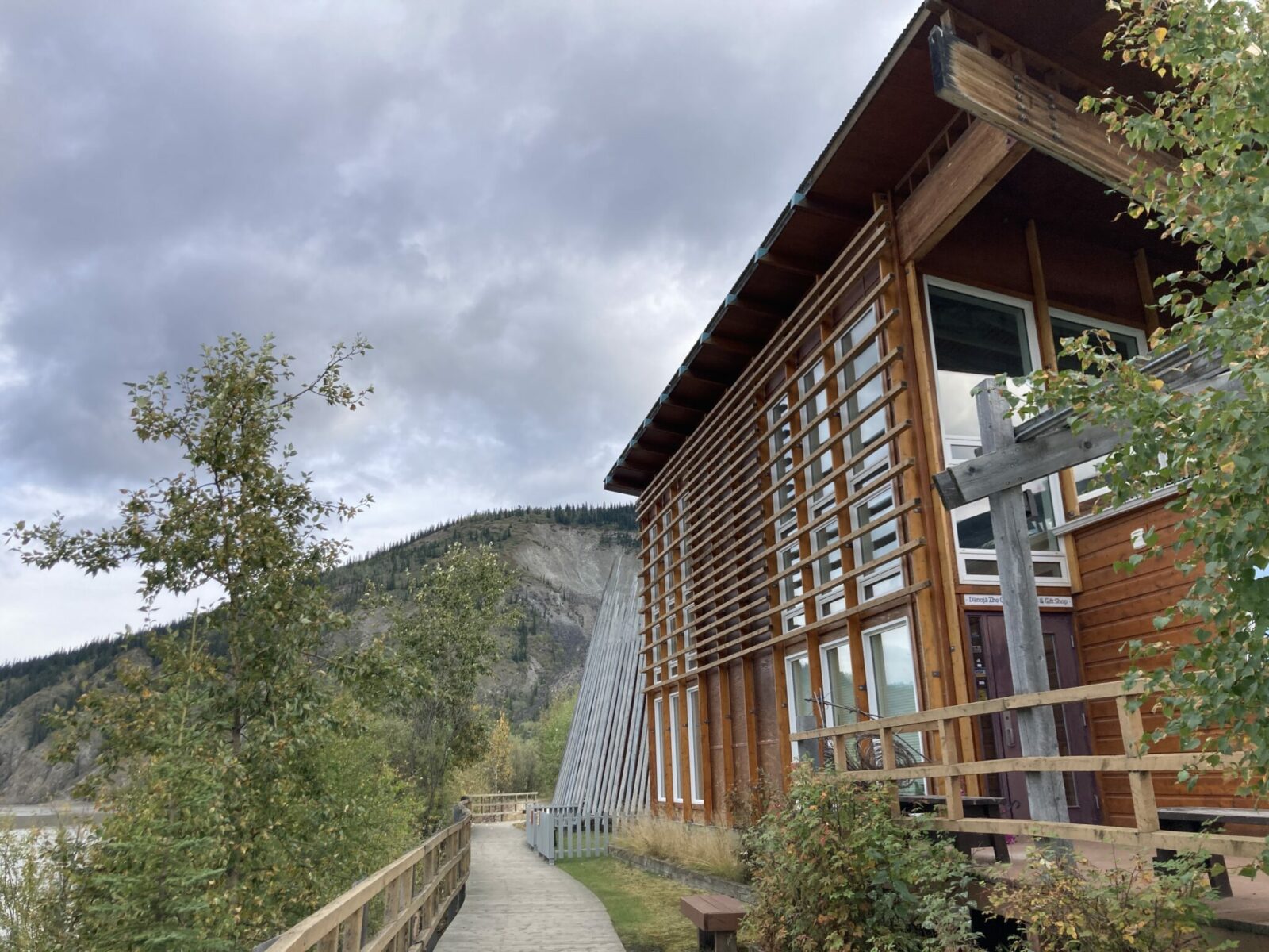 The side of a wood and glass building with a boardwalk around it next to a river