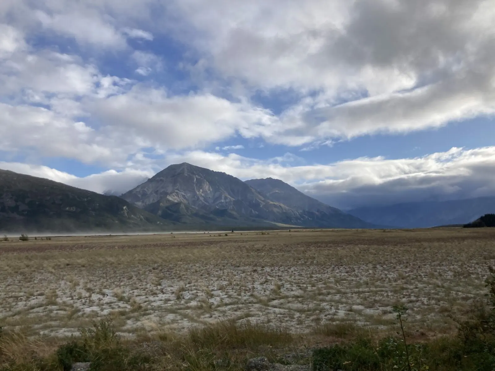 A muddy flat area below beautiful mountains on a partly cloudy day in Kluane National Park on a Yukon road trip