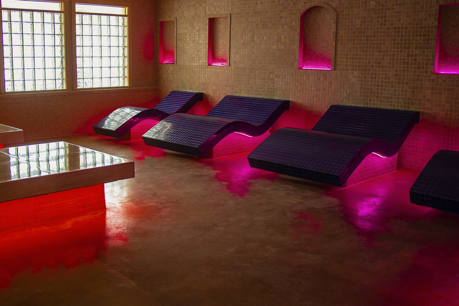 wide tile lounge chairs in a relaxation room with pink lighting.