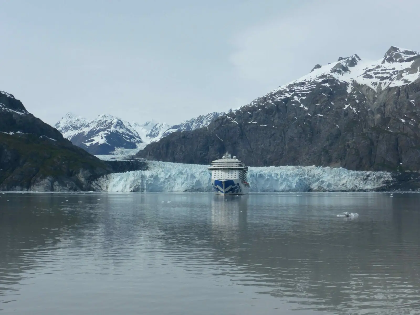 A princess cruise ship in front of a glacier in Glacier Bay National Park, surrounded by mountains on a cloudy day