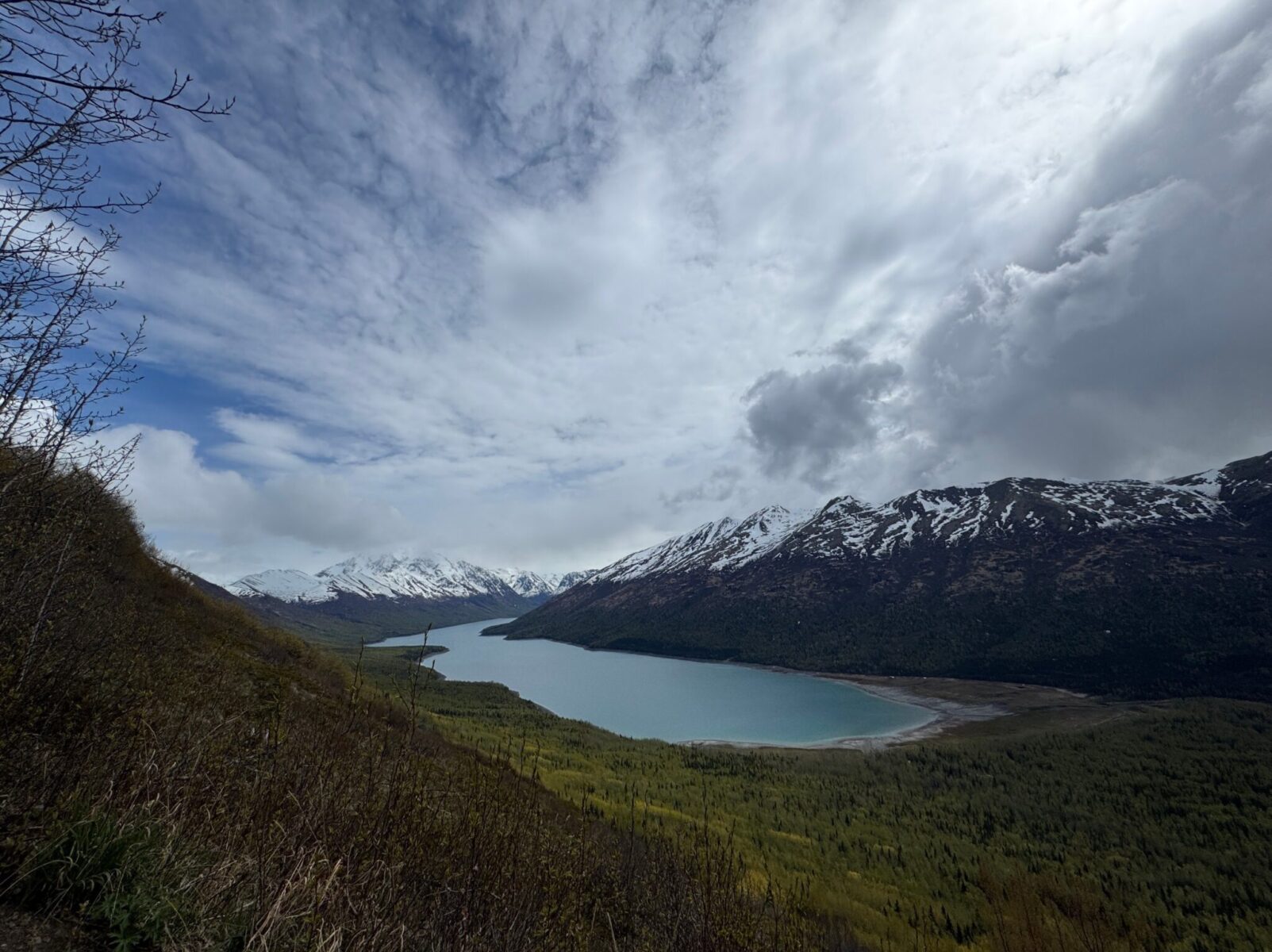 A blue mountain lake surrounded by mountains and forest on a partly sunny day