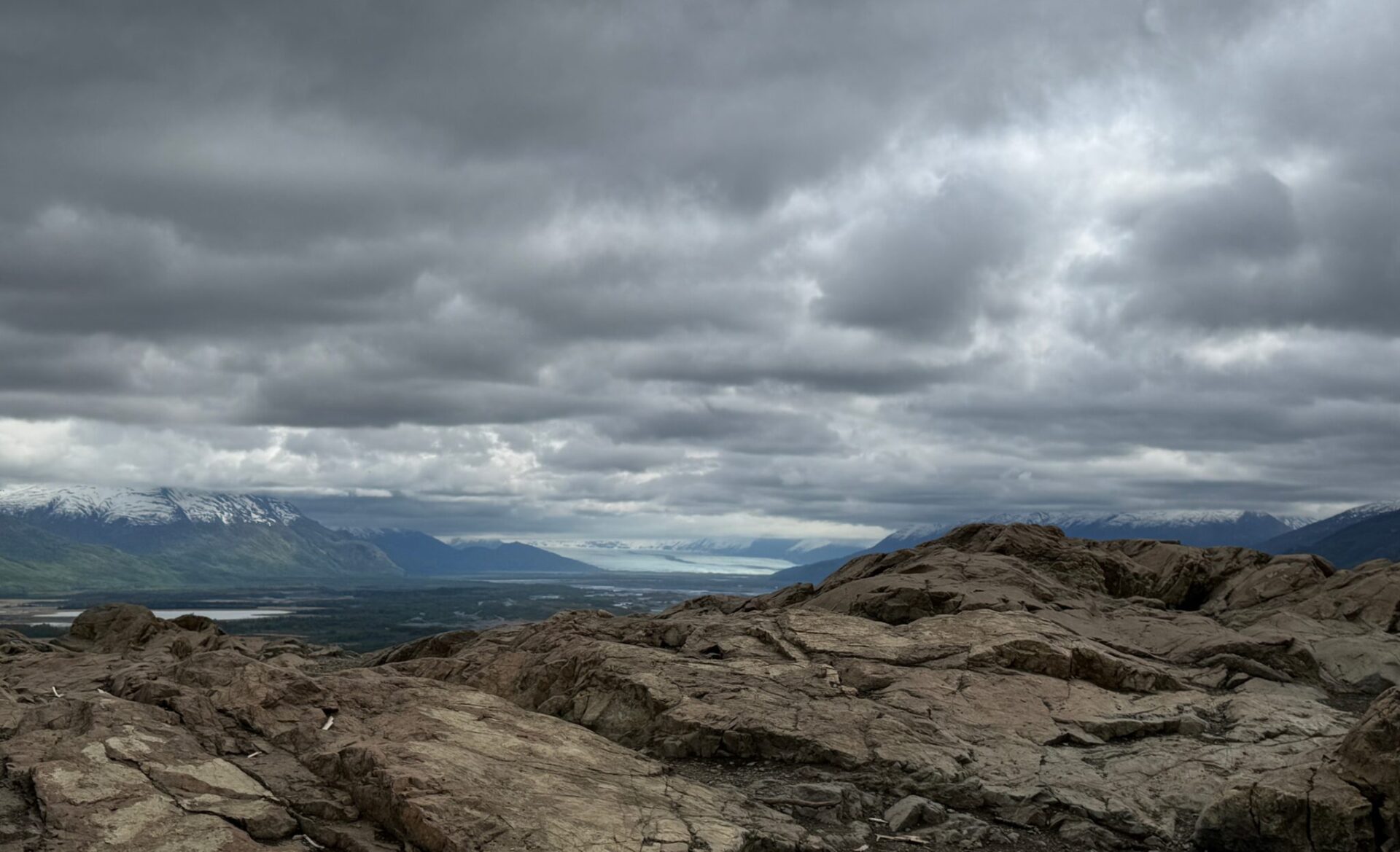 A rocky summit with views of mountains and a glacier on a cloudy day